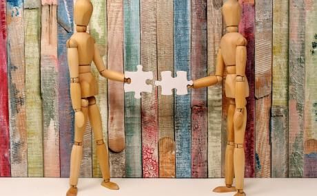 two wooden human figures holding puzzle piece