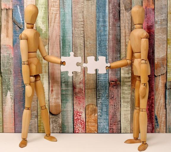 two wooden human figures holding puzzle piece