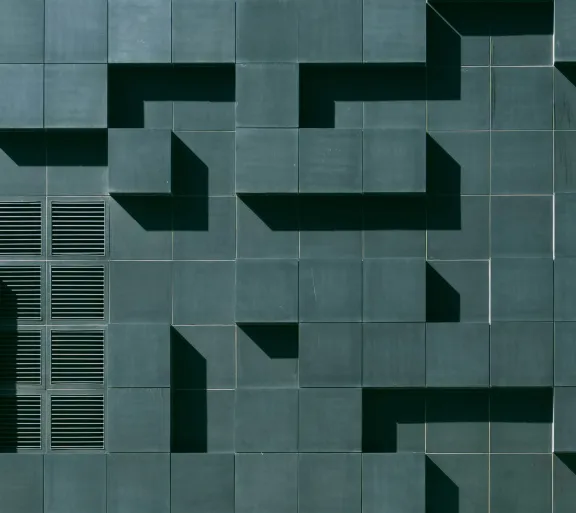 Dark teal wall with various cement blocks jutting outwards creating a horizontal and vertical pattern